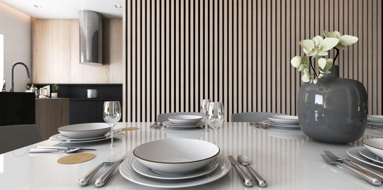 Nowoczesna aranżacja stołu w jadalni z białym, błyszczącym blatem, minimalistyczną zastawą i szarą wazą z białymi orchideami na tle drewnianej ściany z pionowych listew, widoczna kuchnia w tle.