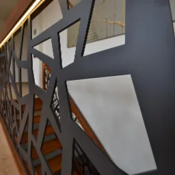 Nowoczesna balustrada schodowa z czarnymi, geometrycznymi wycięciami, podświetlona listwą LED, widok z dołu na drewniane schody i parkiet.