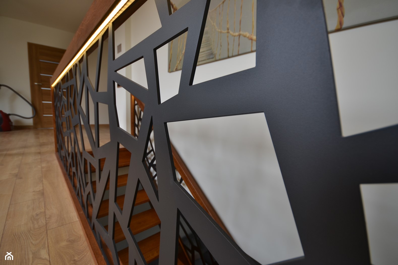 Nowoczesna balustrada schodowa z czarnymi, geometrycznymi wycięciami, podświetlona listwą LED, widok z dołu na drewniane schody i parkiet.