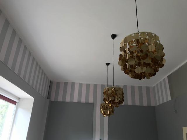 Pokój z trzema złotymi lampami wiszącymi, szarymi ścianami i paskami na górze ścian.