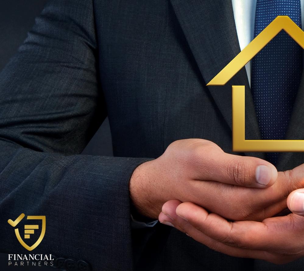 Mężczyzna w garniturze trzyma w dłoniach złoty symbol domu na tle granatowego krawata w kropki.