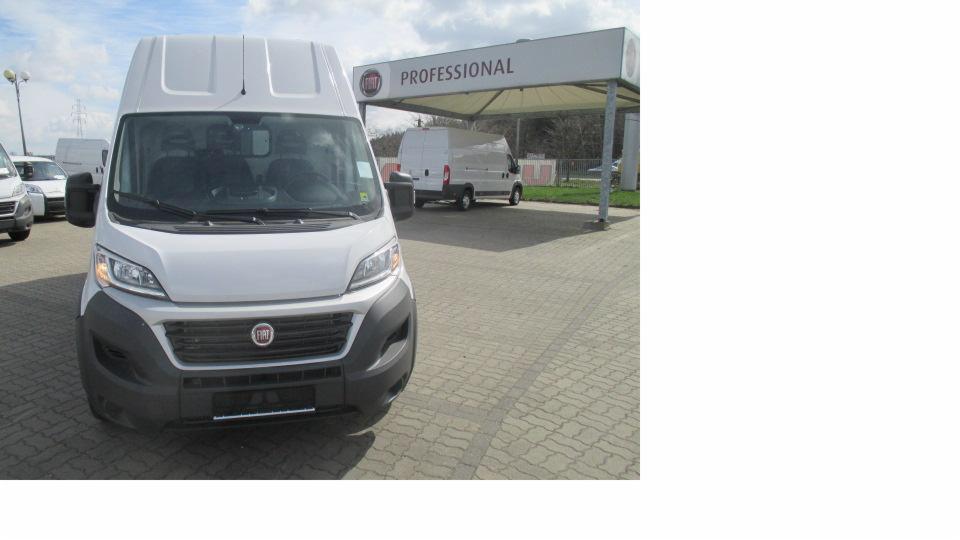 Biały samochód dostawczy Fiat Ducato na placu, widok z przodu, na drugim planie wiata z napisem 'PROFESSIONAL' i kolejny dostawczak.