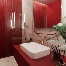 Nowoczesna łazienka z czerwonymi ścianami, marmurowym akcentem i podświetlanym lustrem. Biała, prostokątna umywalka na czerwonej szafce, złota bateria, dyfuzor zapachowy z czarnymi patyczkami...