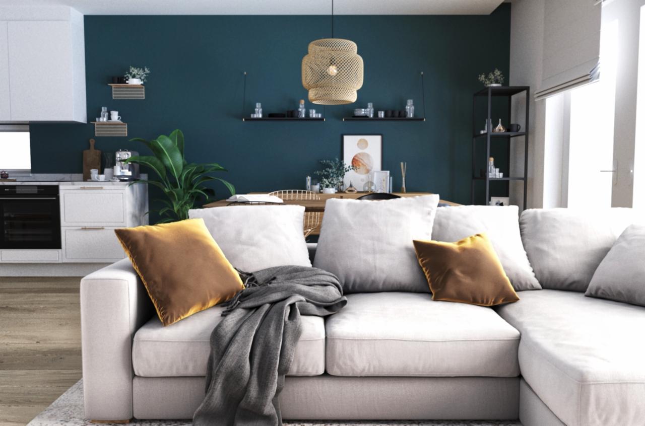 Jasny narożnik z brązowymi poduszkami i szarym pledem na tle ciemnozielonej ściany z półkami i okrągłą lampą wiszącą, widoczna kuchnia w tle.