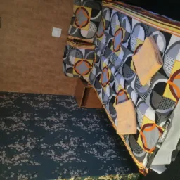 Pokój hotelowy z łóżkiem w geometryczne wzory i dwoma ręcznikami, brązowa ściana oraz dywan w drobne kwiatki