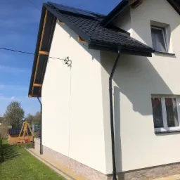 Ocieplona elewacja domu jednorodzinnego w Jeżowem, widok z boku, z widocznym fragmentem ogrodu i placu zabaw w tle.