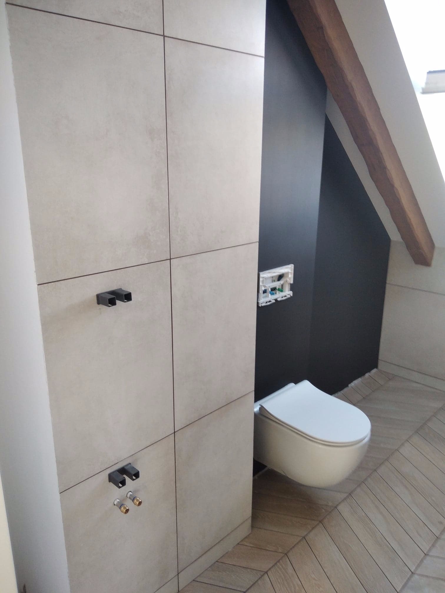 Nowoczesna łazienka na poddaszu ze ścienną toaletą, szarą ścianą i drewnianą belką stropową, wykończona płytkami imitującymi beton w zabudowie geberit.