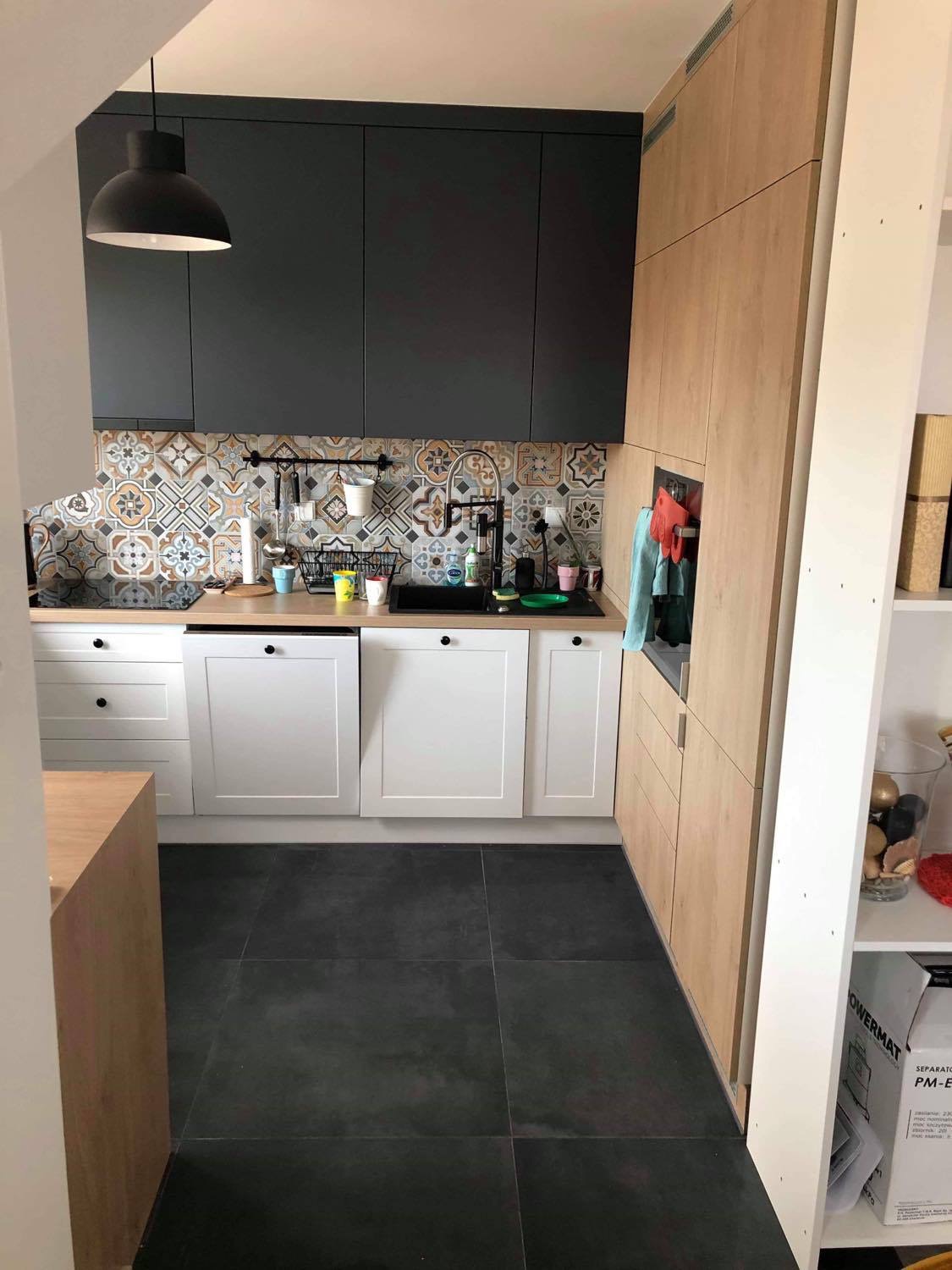 Nowoczesna kuchnia w Jeżowem z czarnymi szafkami górnymi, białymi dolnymi i wzorzystą mozaiką nad blatem, oświetlona wiszącą lampą.