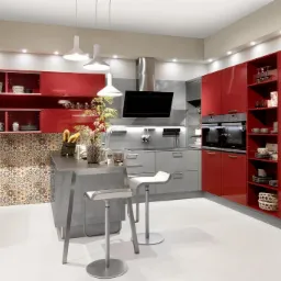 Nowoczesna kuchnia z czerwonymi lakierowanymi szafkami, szarym blatem wyspy i krzesłami barowymi na tle mozaiki ściennej.
