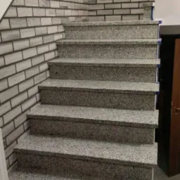 Granitowe schody wewnętrzne z szarymi stopniami i ścianą wyłożoną imitacją cegły, widok z dołu.