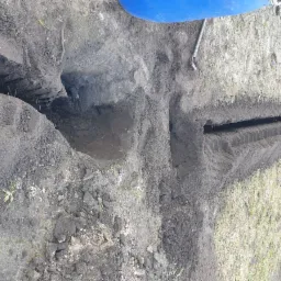 Wykopane rowy w ziemi, prawdopodobnie pod instalację nawadniającą, widoczny fragment niebieskiego zbiornika i zwój żółtego węża ogrodowego.