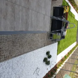 Widok z góry na świeżo założony trawnik z rolki, obrzeża z białych kamieni i szarej kostki brukowej, z widocznymi krzesłami ogrodowymi i drabiną, sugerujący przygotowanie przestrzeni.