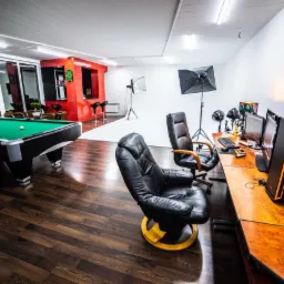 Wnętrze studia z biurkiem montażowym, oświetleniem studyjnym i stołem bilardowym w tle.