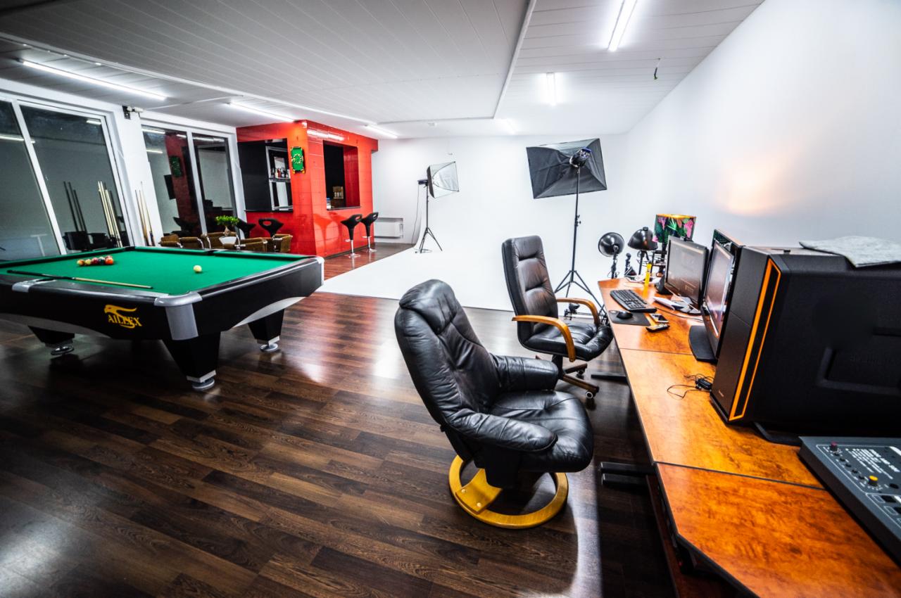 Wnętrze studia z biurkiem montażowym, oświetleniem studyjnym i stołem bilardowym w tle.