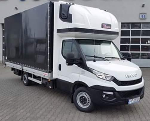 Biały samochód dostawczy Iveco z czarną plandeką na tle szarego budynku z numerem 11 nad bramą.