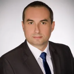 Portret mężczyzny w garniturze z niebieskim krawatem na jasnym tle. Profesjonalny wizerunek biznesowy, neutralny wyraz twarzy, oświetlenie studyjne.