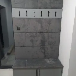 Szara zabudowa przedpokoju z tapicerowanym panelem ściennym, wieszakami i siedziskiem ze schowkiem, nowoczesny design.