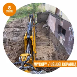 Żółta koparka wykonuje wykop wzdłuż fundamentów budynku, odsłaniając warstwy gruntu i fragmenty starej konstrukcji.