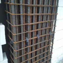 Kosz zbrojeniowy z prętów żebrowanych połączonych drutem i plastikowymi dystansami, ustawiony przy ścianie z białych bloczków.