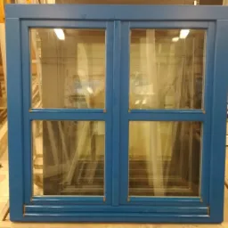 Błękitne okno z szybami, widoczne elementy konstrukcyjne w tle.