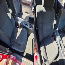 Eco Pranie - Tapicerka samochodowa przed i po czyszczeniu. Widoczne różnice w czystości foteli i podłogi. Ciemna tapicerka z wyraźnym wzorem, czerwone elementy karoserii.