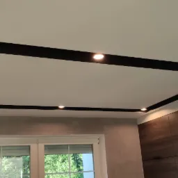 Nowoczesny sufit podwieszany z czarną ramą i punktowym oświetleniem LED w jasnym wnętrzu z oknem.