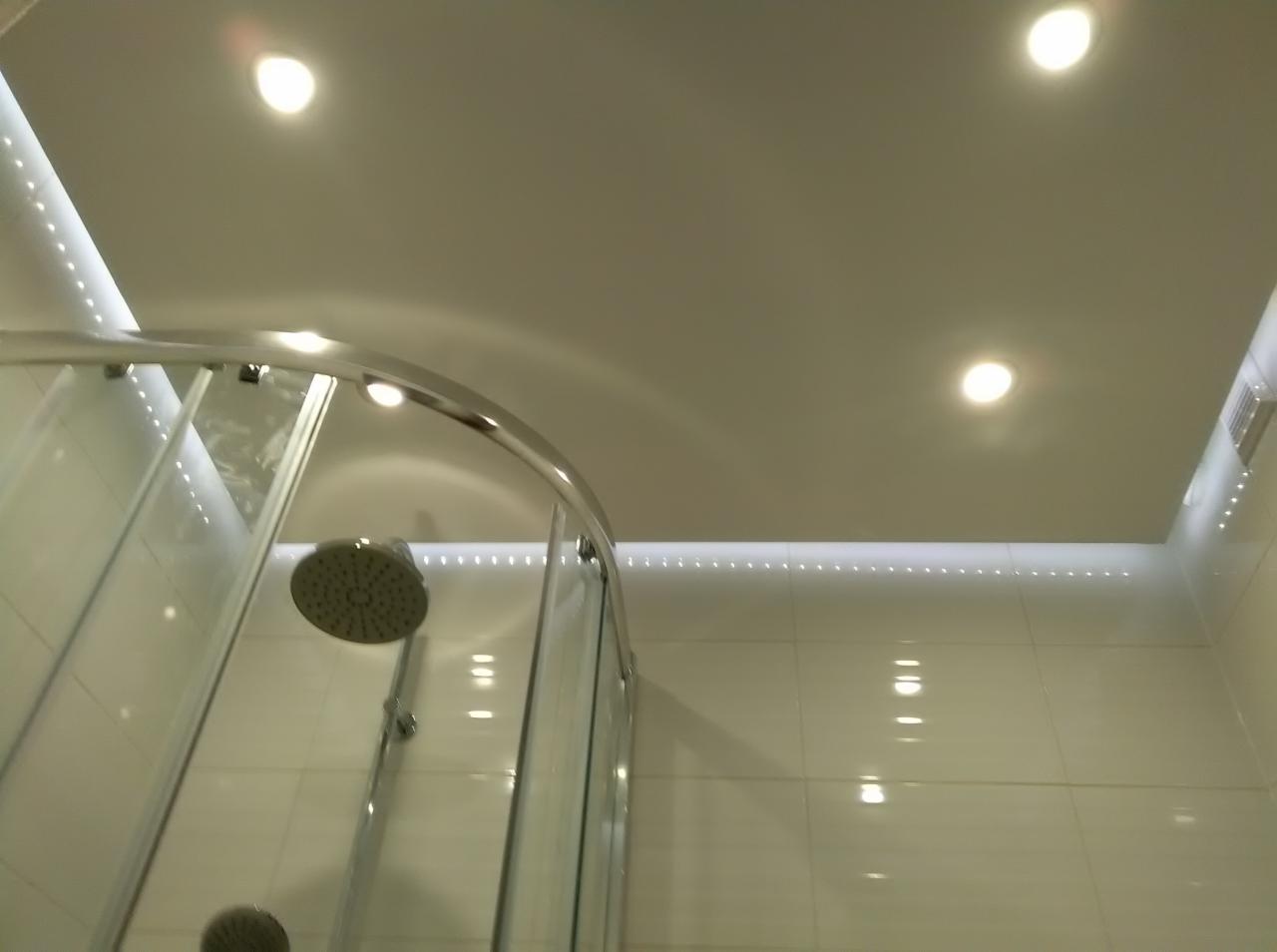 Nowoczesna kabina prysznicowa z chromowanymi detalami, oświetleniem LED podsufitowym i punktowym, białe płytki na ścianach, widok z dołu.