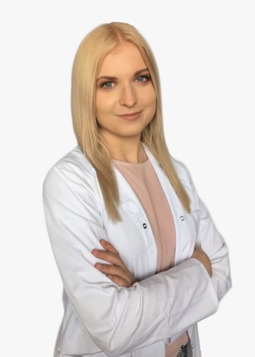 Portret uśmiechniętej kobiety w białym fartuchu medycznym, z założonymi rękami, świadczącej usługi w Warszawie. Jasne blond włosy i delikatny makijaż.