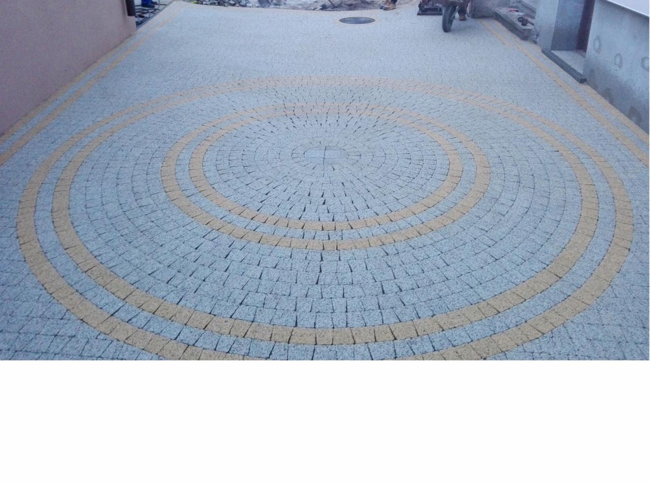 Ułożona kostka granitowa w kształcie spirali z dwóch kolorów, szarego i beżowego, na podjeździe przed domem.