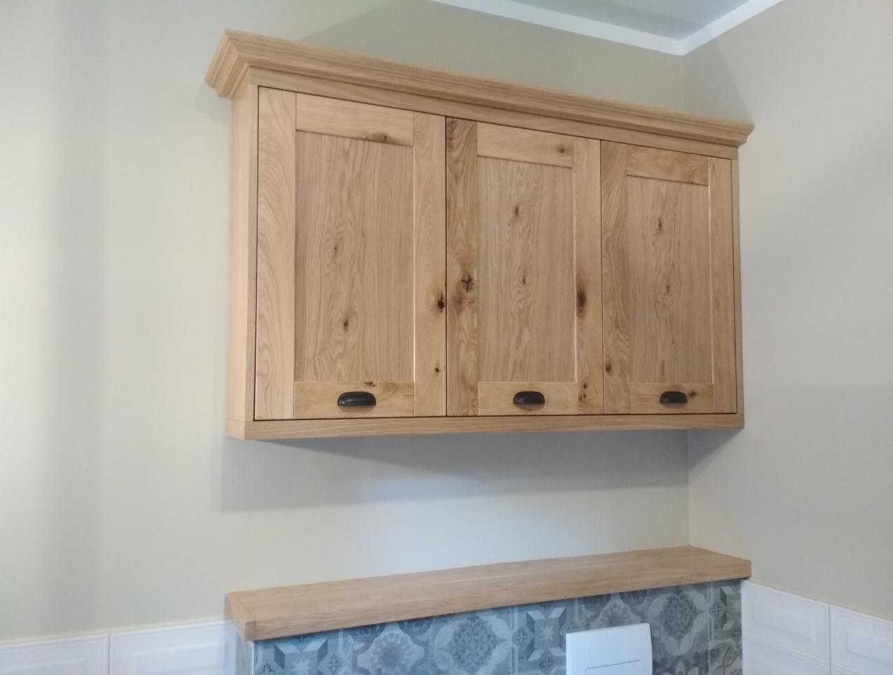 Wisząca szafka kuchenna z drewna dębowego z trzema frontami, z czarnymi uchwytami, nad blatem w dopasowanym odcieniu drewna i wzorzystymi płytkami.