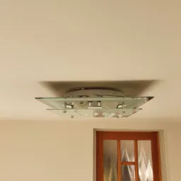 Szklany plafon sufitowy z elementami dekoracyjnymi, widoczny na tle białego sufitu i fragmentu drewnianych drzwi z szybami.