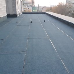 REGION BUD SP. ZO. O. - Płaski dach pokryty papą termozgrzewalną z widocznymi odpowietrznikami, budynki mieszkalne w tle.