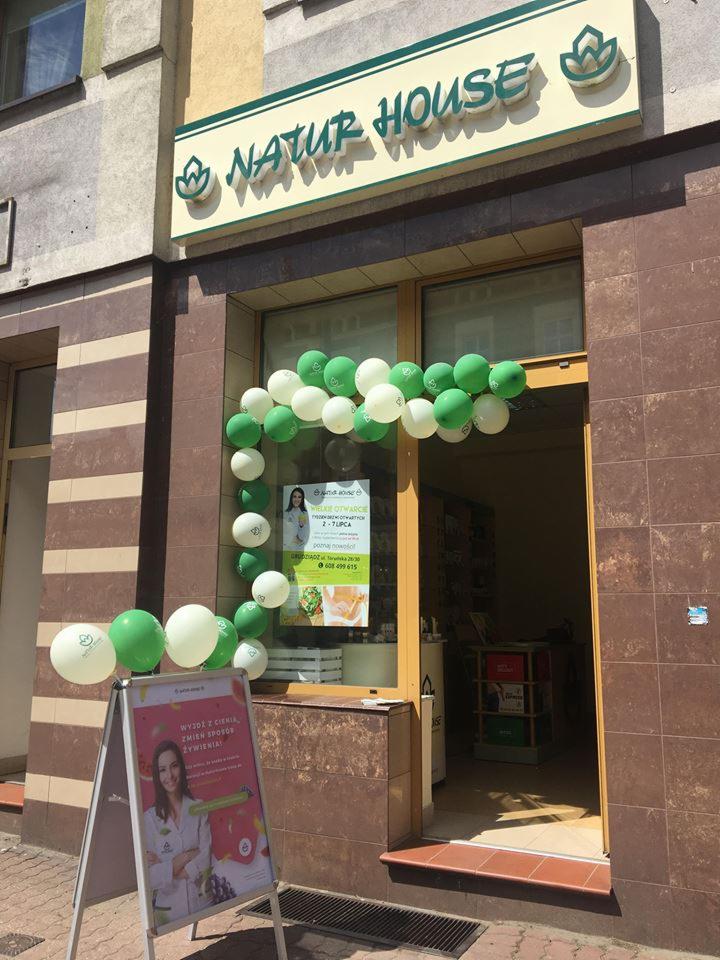 Fasada budynku Natur House udekorowana zielono-białymi balonami z okazji otwarcia, widoczny plakat reklamowy z uśmiechniętą kobietą i hasłem o zmianie sposobu żywienia.