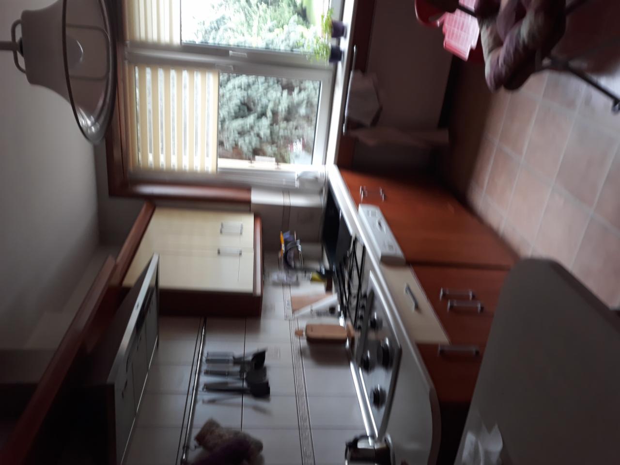 Wnętrze kuchni z oknem, widoczne szafki, kuchenka i blat, z perspektywy lekko z góry, po remoncie.