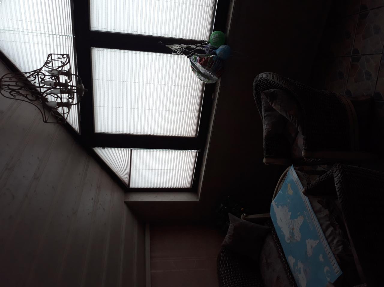 Okno dachowe z żaluzjami plisowanymi, dekoracyjna lampa sufitowa i elementy wystroju wnętrza w ciemnym pokoju.