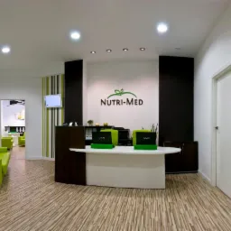 Recepcja gabinetu dietetycznego Nutri-Med z logo na ścianie, zielonymi akcentami i laptopami VAIO, widok na poczekalnię z zielonymi sofami.