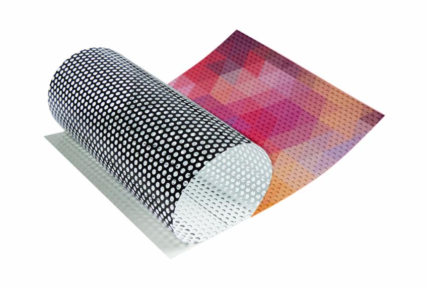 Rolka perforowanej folii okiennej z czarnymi kropkami na białym tle, częściowo odklejona od arkusza z geometrycznym wzorem w odcieniach różu i pomarańczy, prezentacja produktu.