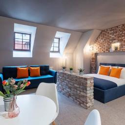 maciejschulz.com - Pokój hotelowy z ceglaną ścianą, niebieską sofą i łóżkiem, białym stołem z kwiatami i oknami na poddaszu.