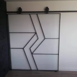 Nowoczesne, przesuwne drzwi w stylu loftowym z czarną, geometryczną ramą na tle białej ściany i czarnej ściany o fakturze kamienia.