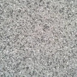 Szara, drobnoziarnista faktura ściany z widoczną strukturą nakrapianą, przypominającą tynk mozaikowy.