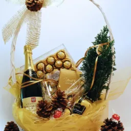 Elegancki kosz prezentowy z szampanem, pralinkami Ferrero Rocher i Lindt, likierem jajecznym, ozdobiony szyszkami i małą choinką, przewiązany złotą wstążką.