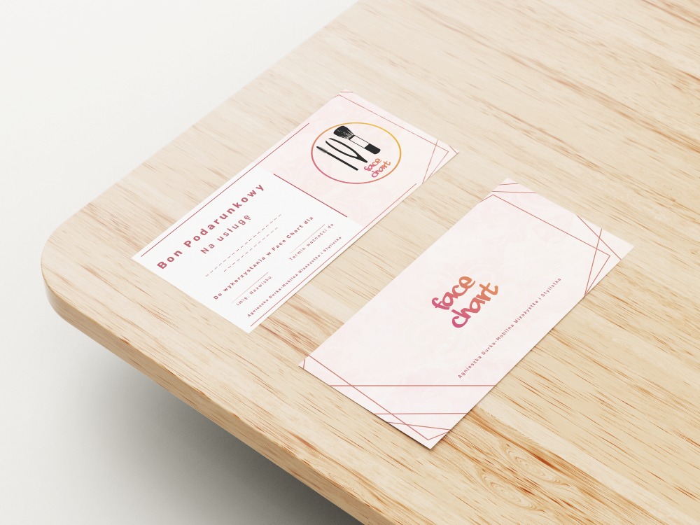 Bon podarunkowy i wizytówka salonu makijażu Face Chart leżące na drewnianym blacie. Na bonie widnieją grafiki pędzli do makijażu.