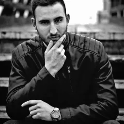 Czarno-biały portret młodego mężczyzny w skórzanej kurtce, siedzącego na schodach z zamyśloną miną i zegarkiem na nadgarstku.