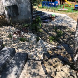 Weles Patryk Macięga - Ogród z białym żwirem, kamiennymi płytami wokół brzozy i schodami. W tle plac zabaw i budynek z instalacją gazową. Estetyczne zagospodarowanie przestrzeni.