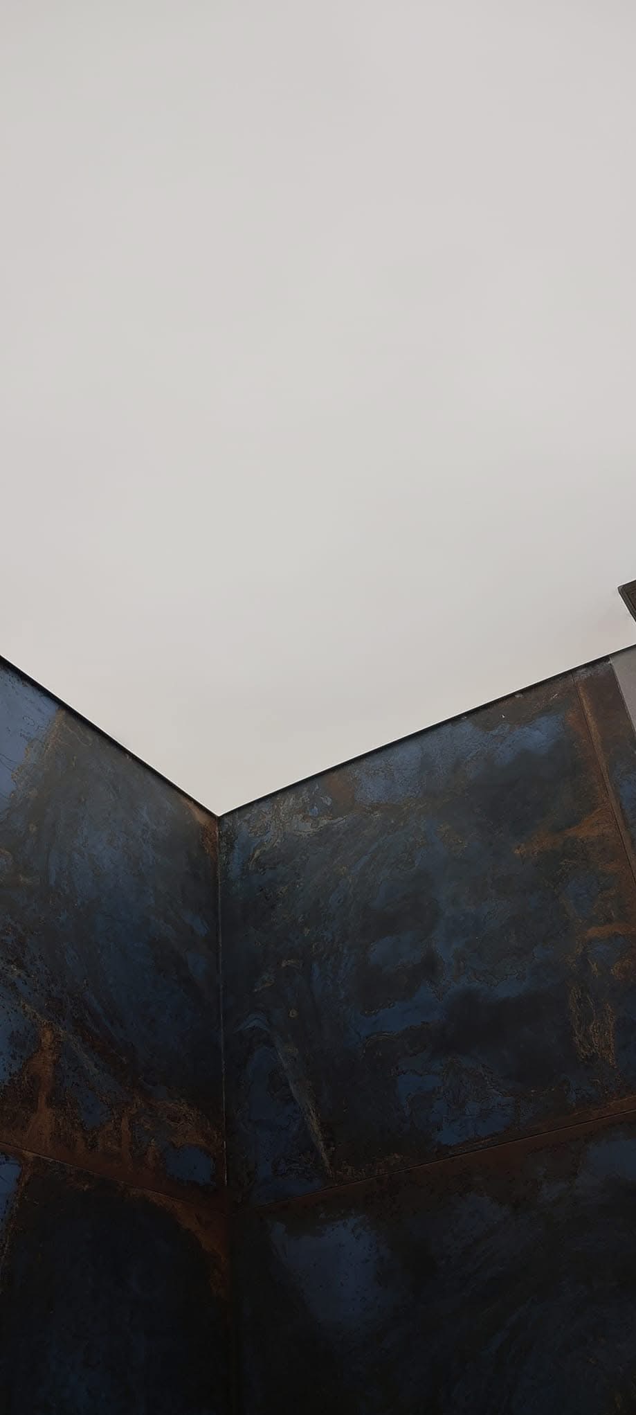 Błękitno-rdzawy sufit napinany z efektem marmuru, widoczny z dołu, podkreślony przez białą powierzchnię sufitu w tle.