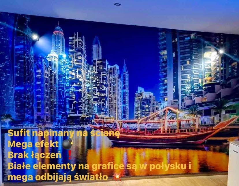 Sufit napinany na ścianie z grafiką nocnego miasta i łodzi. Białe elementy grafiki połyskują i odbijają światło. Bez łączeń na powierzchni.