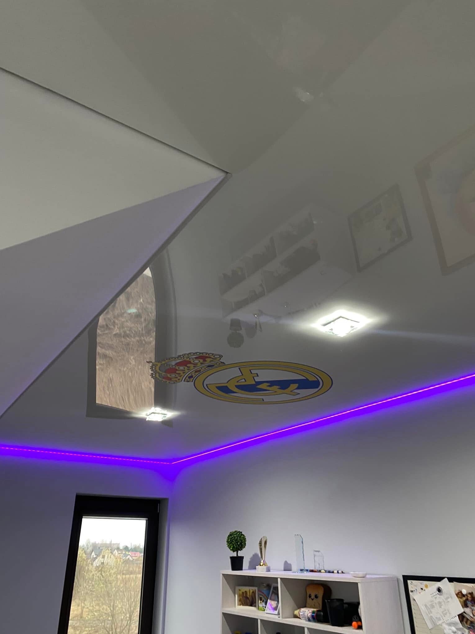 Biały sufit napinany z nadrukiem herbu klubu sportowego i fioletowym oświetleniem LED w pokoju, Sosnowiec.