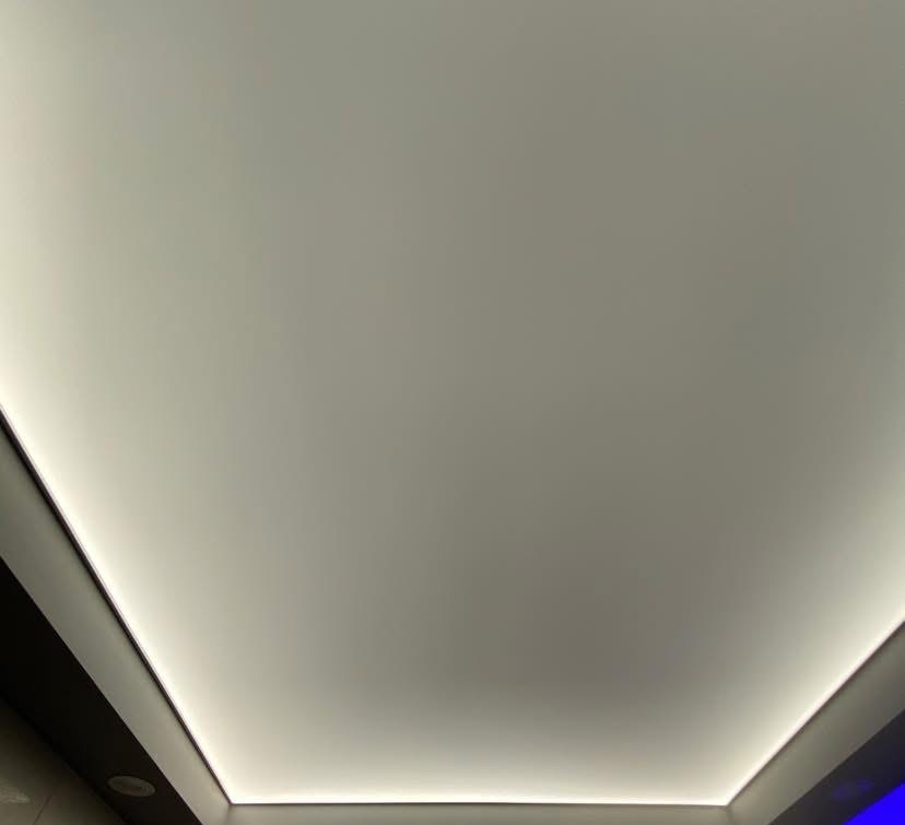 Gładka, biała powierzchnia sufitu z subtelnym oświetleniem LED po obrysie, tworzącym nowoczesny efekt wizualny. Minimalistyczny design.