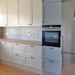 Jasna kuchnia z drewnianym blatem, szarym wykończeniem ściany i sprzętem AGD marki Siemens.