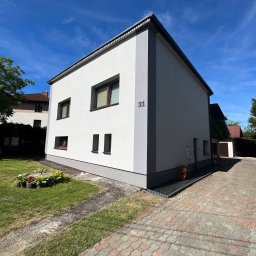 Docieplenia&elewacje - Dwukondygnacyjny dom z numerem 31, otynkowany na biało z szarymi akcentami, widoczny z zewnątrz w słoneczny dzień, z brukowanym podjazdem i małym klombem.